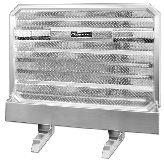 Front view of a deluxe aluminum truck storage box with a diamond‑plate face panel, horizontal reinforced ridges, integrated locking access panels, and raised support legs, featuring a Zamzow logo, isolated on a white background.
