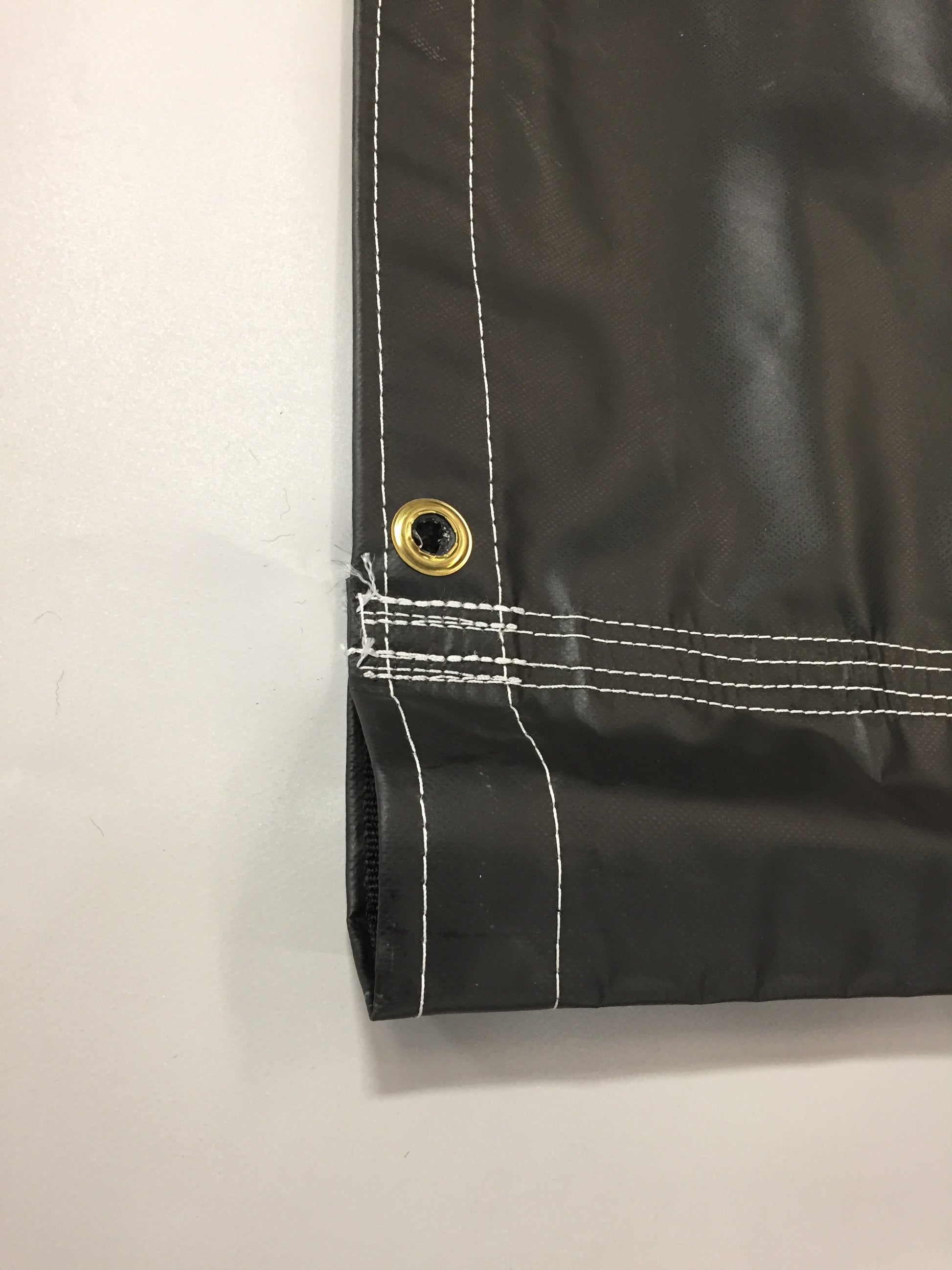 Close-up of a black fabric with white stitching and a gold grommet on a light gray background